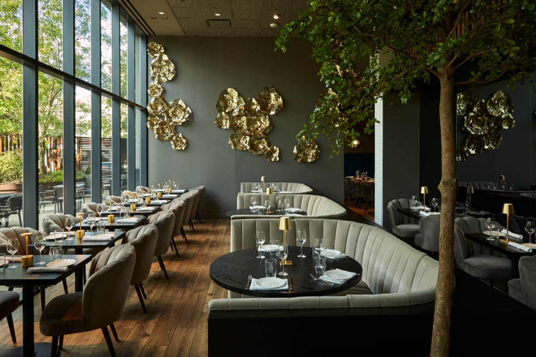 A speaker on a stage in a ballroom, presenting in front of a large screen that displays "Product School" and an image related to "Product Manager." The stage is lit with blue and white lights, and a banner for "Product School Silicon Valley" is visible.